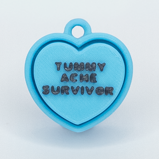 Blue heart-shaped pendant with 'Tummy Ache Survivor' text on a light blue background